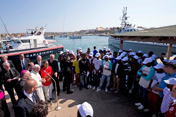 Pope Francis speaks to migrants, wearing white caps, during his visit to the island of Lampedusa, southern Italy, to show solidarity with migrants.