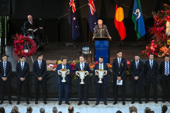 Mark Thompson, Joel Selwood and Chris Scott hold their premiership cups on stage at the memorial for Costa.