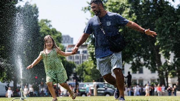 Portuguese tourists Miriam and her dad cool down in a sprinkler in Parliament Square, London.