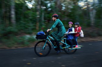 Melissa Derwent with her daughters,  Sophie, 7, (centre) and Natalie, 4, riding their electric cargo bike in Oatley, NSW. 