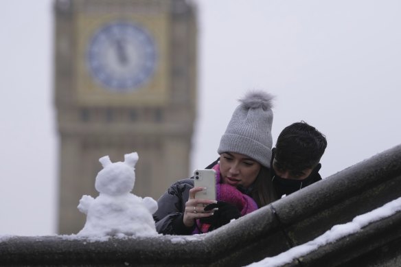 A couple take a photo of a snowman in London on Monday December 12.