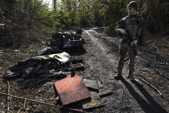 An Ukrainian soldier looks at the decomposed body of a Russian soldier lying on the ground on October 1, 2022 in Kupiansk, Ukraine. 