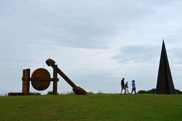 People walk past Morgan Jones’ Early Light (left) and Tony Davis’ Folly Interstice which are part of the Sculpture by the Sea exhibition.