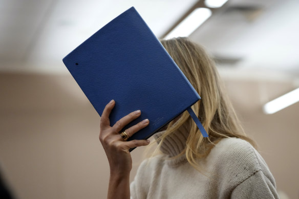 Gwyneth Paltrow shields her face with a blue notebook as she exits a courtroom.