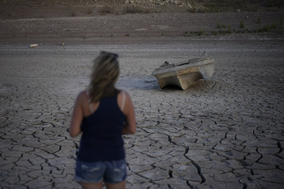 A woman looks at a formerly sunken boat now on cracked earth hundreds of feet from what is now the shoreline on Lake Mead.