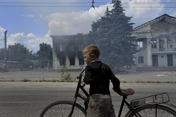 Eight-year-old Timosha stands with his bicycle in front of the burning Palace of Culture in Lysychansk. The city is now occupied by Russia.