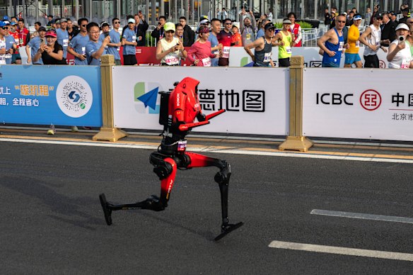 
An Honor H1 humanoid robot running beside human runners at the start of the Beijing Humanoid Half Marathon. 
