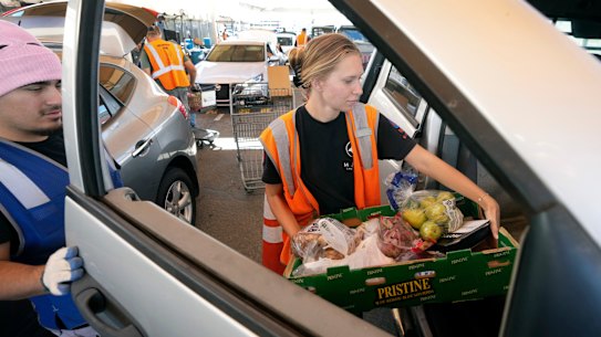 St. Mary’s Food Bank of Arizona volunteer Kayli Iverson, right, and Josh Torres, left, a St. Mary’s Food Bank employee deliver food to a car at the main facility in Phoenix on Tuesday.
