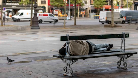 A homeless person sleeps on a bench in downtown Paris.