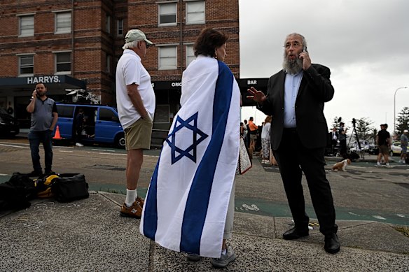 A woman draped in the Israeli flag stands with Rabbi Mendel Kastel who lost multiple family members.