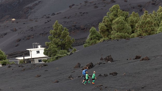 A family walks up a hill to a football field in the Las Manchas area of La Palma through an area entirely carpeted with volcanic ash.