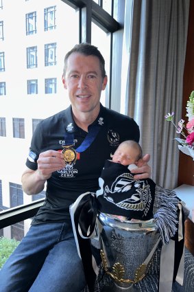 Collingwood coach Craig McRae with his newborn daughter Maggie and the premiership cup and medal on Monday.