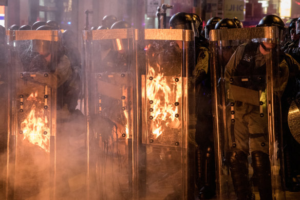 Riot police stand in front of a barricade set on fire by protesters after dispersing crowds outside the Mong Kok Police station in Hong Kong on Friday evening.