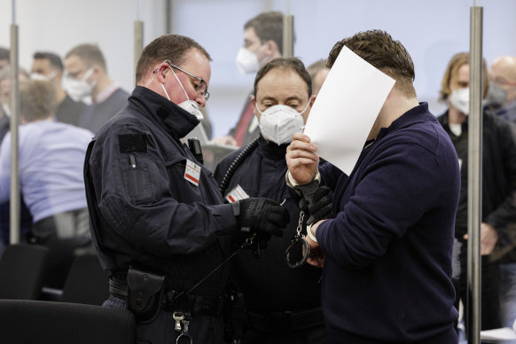 The defendant hides his face as he is led into a courtroom of the Higher Regional Court in Dresden. 