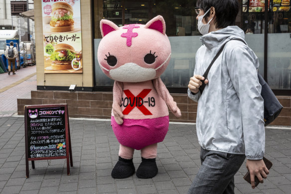 A costumed character reminds passersby in Tokyo of the dangers of COVID.