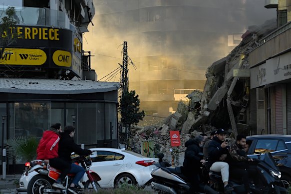 I residenti nel sud di Beirut passano davanti alla scena di un recente attacco aereo israeliano. 