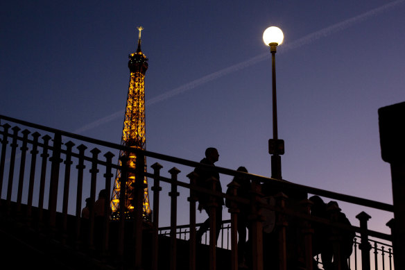 Işıklar söndü: İnsanlar Paris'teki Eyfel Kulesi'nin yanındaki bir köprüde yürüyor.