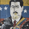 Pedestrians wearing protective masks walk by a mural of President Nicolas Maduro in Caracas, Venezuela, on Tuesday.