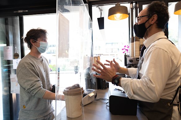 Valerio Domenici serves a customer from behind a perspex screen in his cafe, Zuchero Caffe, in Artarmon, Sydney.