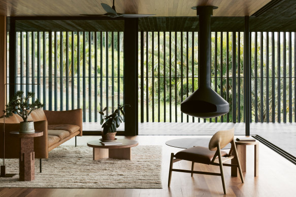 Large sliding glass doors connect the living area with a verandah screened by black battens. Inside, warmth is created by a natural colour palette provided by timber-lined ceilings and floors, leather furniture, including a Fogia “Tiki” sofa by Andreas Engesvik, and suspended fireplace.