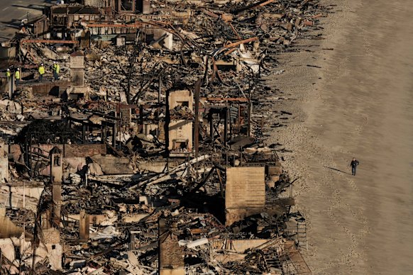 A person walks on the beach next to homes destroyed by the Palisades fire. 