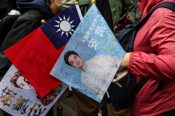 A KMT supporter holding a Taiwanese flag, Chiang Wan-an flag, and a flag with photos of Chiang and his great grandfather Chiang Ching-kuo ahead of the local elections.