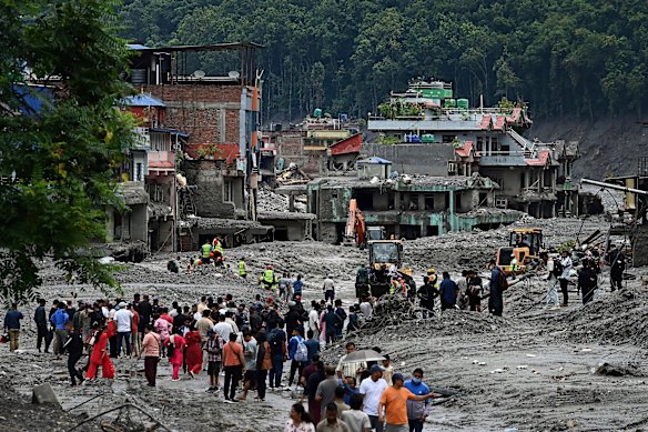 A crowd gathers as workers use heavy machinery  to start clearing debris from the ruins of Dhunge in Nepal, August 29.
