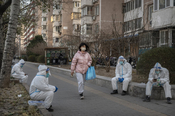 A pedestrian walks by epidemic control workers in Beijing. 