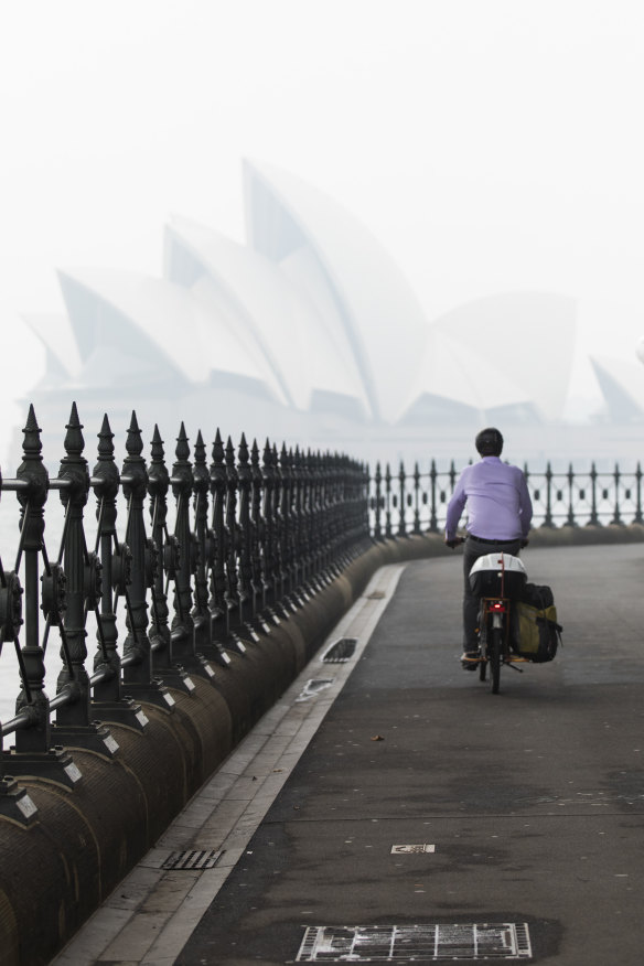A cyclist rides by Sydney Harbour with the Opera House barely visible in the distance.