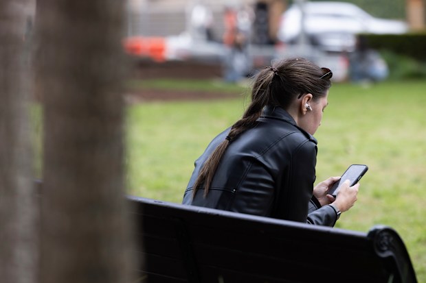 Bir kadın parkta bankta oturarak telefonunu kullanıyor