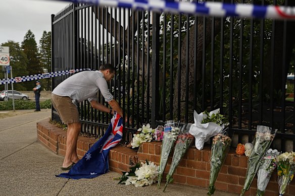 A man ties an Australian flag to a fence near one of the impromptu memorials near the crime scene.