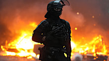A police officer wearing riot gear stands in front of a burning barricade during a demonstration near Place de la République,