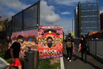 People walk past a mural with the Aboriginal flag that welcomes people to the Block on Eveleigh Street in Redfern.