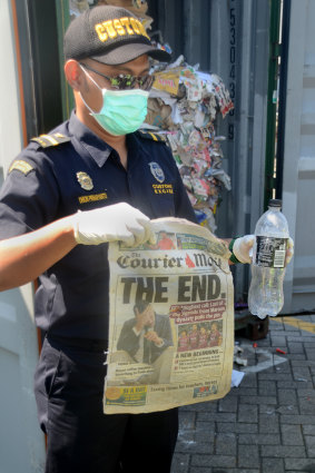 Indonesian Customs offical Dhion Priharyanto holds up a copy of an Australian newspaper among other rubbish in a rejected container.
