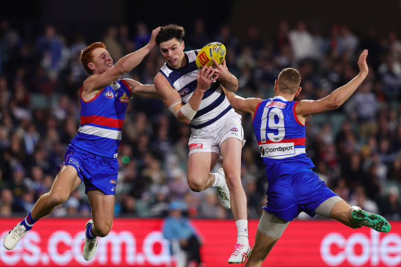 Oliver Henry of the Cats marks the ball in between Ed Richards of the Bulldogs and Liam Jones of the Bulldogs.