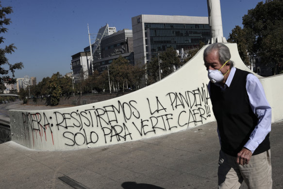 A man wearing a face mask walks past graffiti against Chilean President Sebastian Piñera that reads in Spanish "Piñera, we will resist the pandemic just to see you fall!" in Santiago.