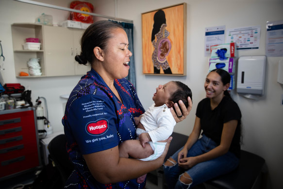 Midwife Mel Briggs, wearing the “Sister Scrubs” to identify herself as Indigenous, Yuin woman Hayley Williams and baby Jaari.