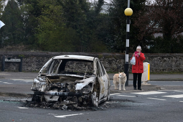 A woman takes a photograph of a burnt-out car at Cloughfern, following  loyalist violence in Belfast, Northern Ireland.
