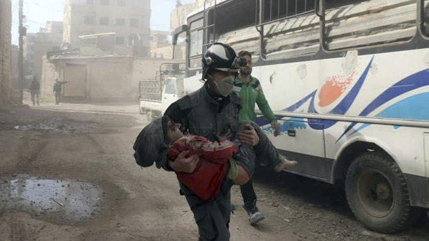 This pictue provided by the Syrian Civil Defence White Helmets shows a member of the Syrian Civil Defence group carrying a boy wounded during airstrikes and shelling by Syrian government forces in Ghouta on Friday.