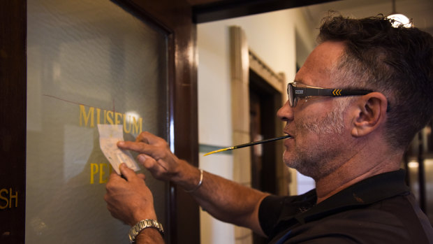 Mr Haines applies gold leaf to the museum's logo on one of the glass doors. 