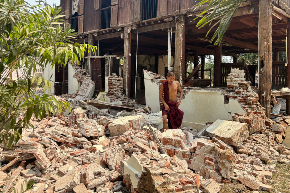 A Buddhist monk walks near a damaged building at a monastery compound.