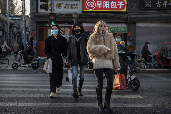 Women, some not wearing masks, cross a road near closed shops in Beijing on Sunday.