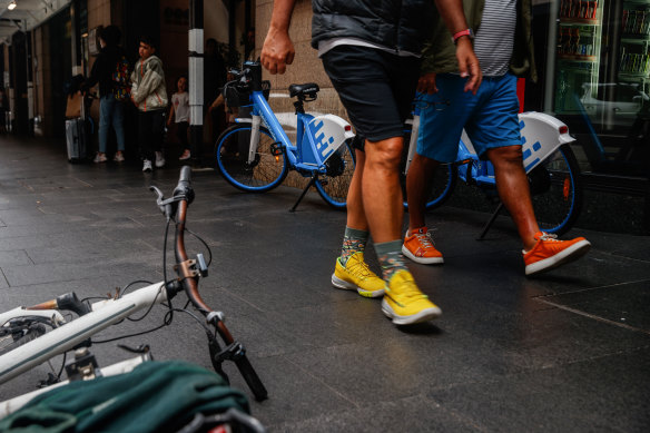 Pedestrians walk past HelloRide ebikes parked in the Sydney CBD in early January 2023.