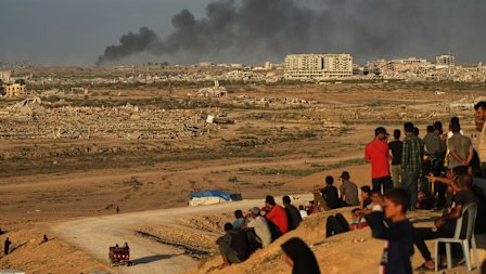 Displaced Palestinians watch smoke rise after Israeli military strikes as they gather on the coastal road near Wadi Gaza, in the central Gaza Strip, on Thursday