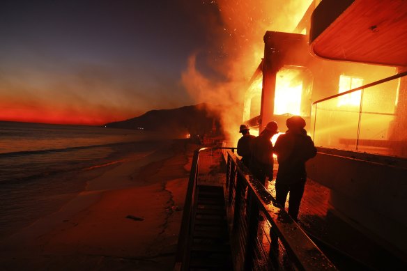 Firefighters work from a deck as the Palisades fire burns a beachfront property in Malibu.