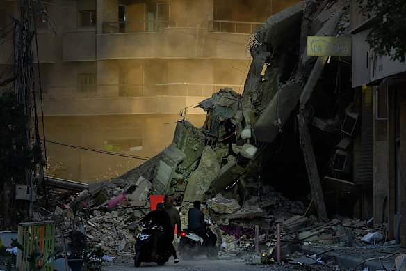 La gente cammina vicino alla scena di un attacco aereo israeliano nel sud di Beirut. 