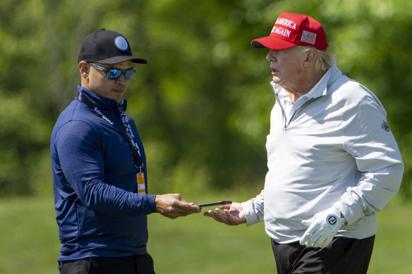 Walt Nauta, left, takes a phone from former president Donald Trump during the LIV Golf Pro-Am at Trump National Golf Club in May.
