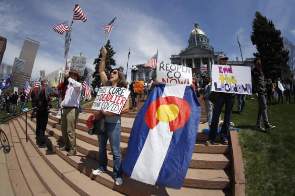 Protesters wave placards and flags as they stand on the west steps of the State Capitol during a protest against the stay-at-home order issued by Colorado Governor Jared Polis.