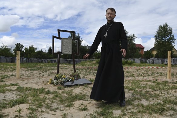 Father Andriy Halavin stands at the rear of the church, in front of the memorial and plaque at the site of the mass grave of civilians killed by Russian soldiers.