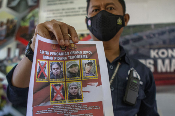 A police officer shows a wanted poster displaying the photos of two militants Ali Kalora, top left, and Jaka Ramadan, bottom left, who were killed during a shootout with security forces.